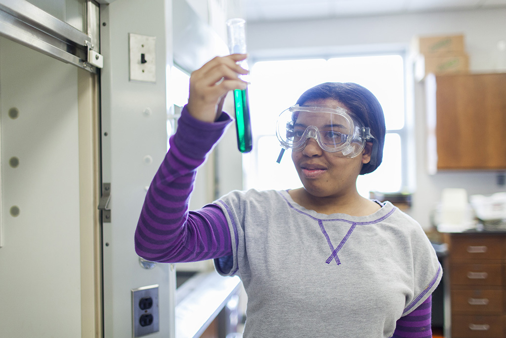 Female student looking at a test tube with a green luquid in it. 