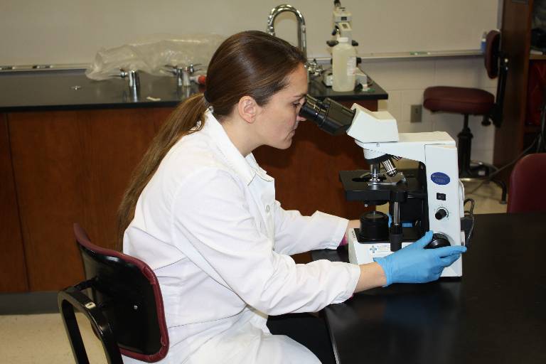photo of a female medical student looking through a microscope in a lab