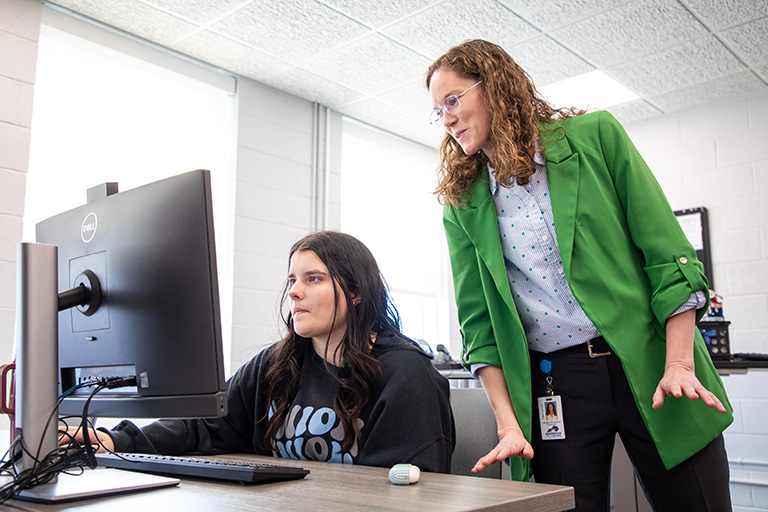 an instructor helping a student in front of a computer during class