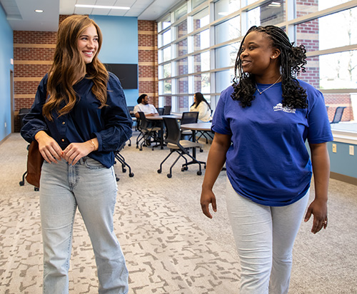 two girls walking inside a college hall