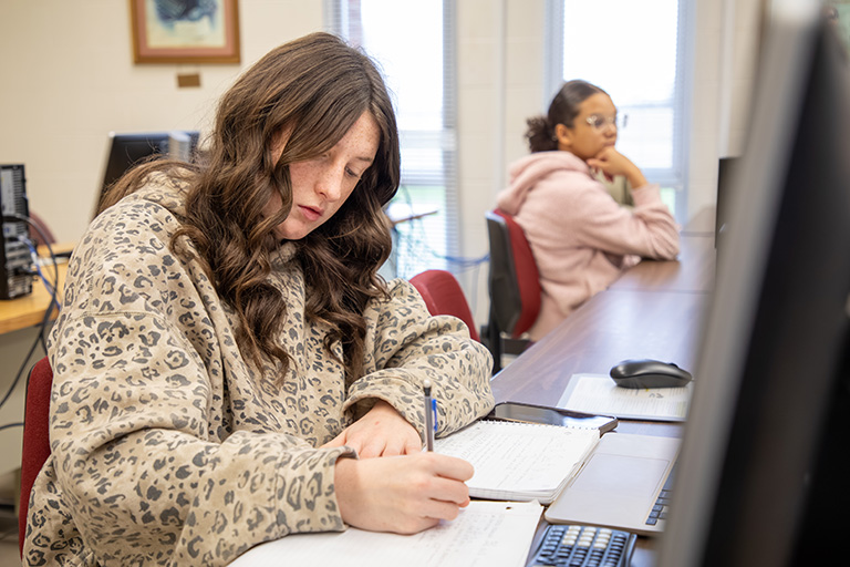 female student writing on a desk by computer