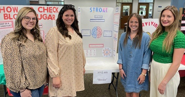 female students standing in front of a presentation board
