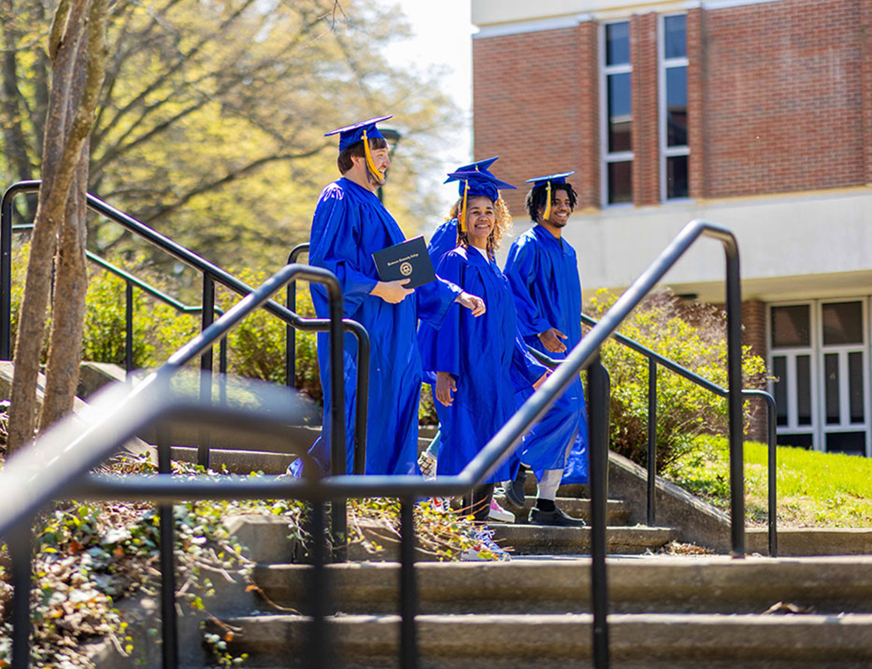 students in graduation attire walking outside the HCC campus