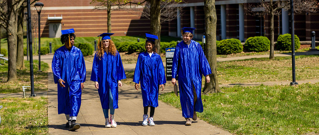 Four students in graduation regalia walking across the HCC campus