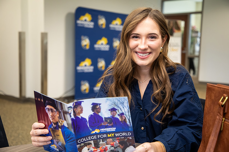 a female student sitting at a desk and holding a campus brochure