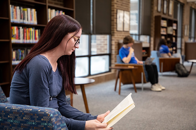 a student reading a book sitting in a chair