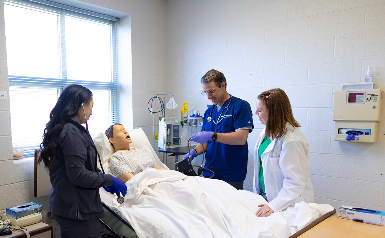a nursing instructor working with two students in a clinical lab