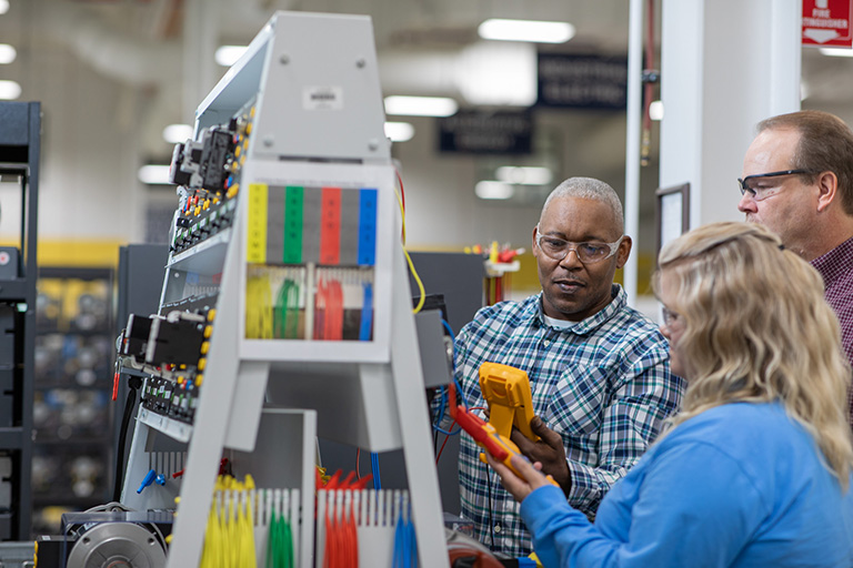 two men and a woman working with an electronics board